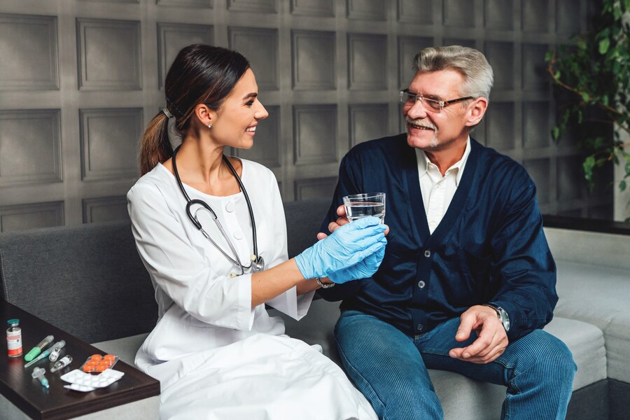 Smiling young female doctor hands a glass of water to an older man, helping and caring for an elderly person